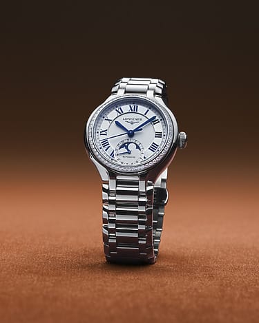 Silver analog wristwatch with blue Roman numerals and stainless steel band on a brown gradient background.