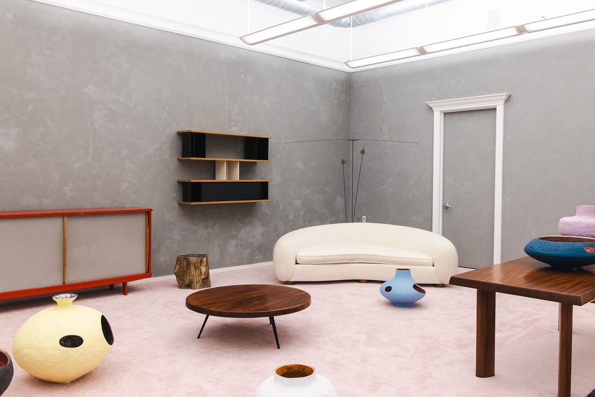 Modern living room with gray walls, minimalist furniture, a white curved sofa, unique wooden table, and colorful ceramic decor.