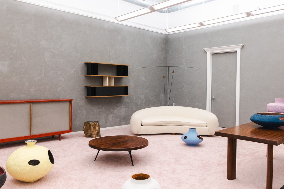 Modern living room with gray walls, minimalist furniture, a white curved sofa, unique wooden table, and colorful ceramic decor.