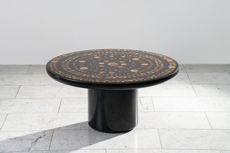 Round black table with intricate wood inlay design on a marble floor background.