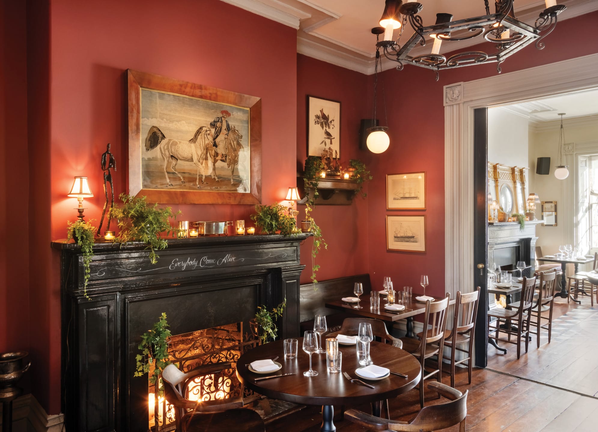Cozy restaurant with red walls, a fireplace, elegant table settings, and framed artwork.