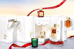 advent calendar with perfume bottles, chocolates, and a candle on a reflective surface with a red ribbon