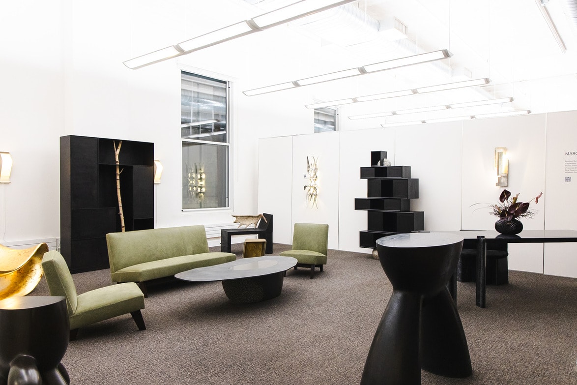 Modern interior with green sofas, unique black furniture, and decorative lighting in a bright, open gallery space.