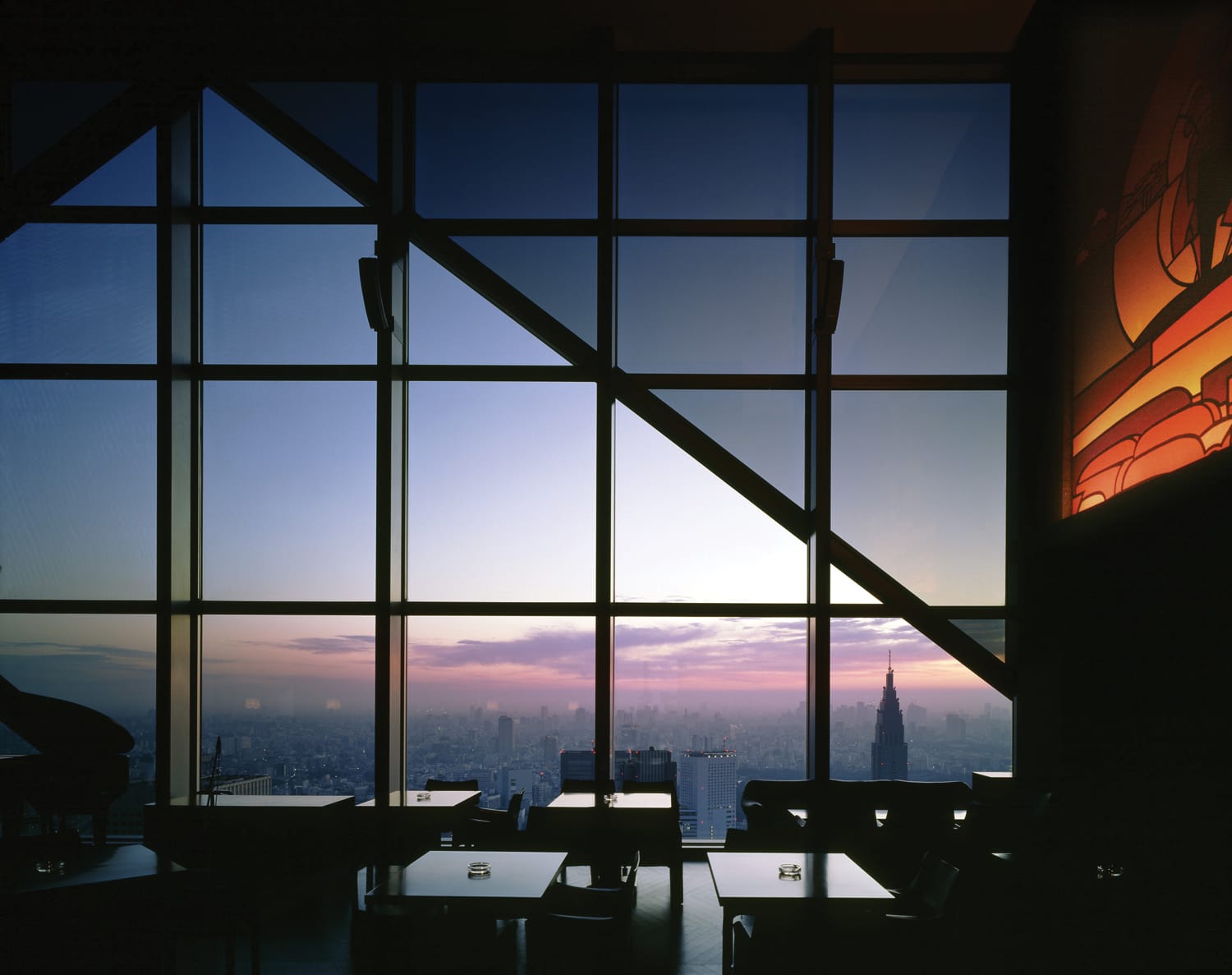 Silhouette of a city skyline through large windows at sunset with furniture in the foreground.