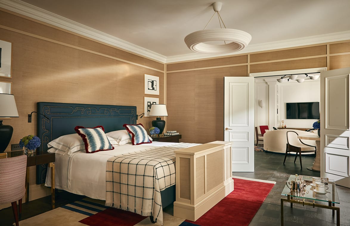 Elegant hotel room interior with a neatly made bed, modern decor, and an open door leading to a cozy seating area.