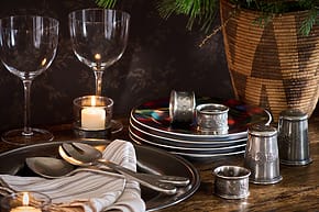 Elegant dinner setup with wine glasses, striped napkins, plates, metal utensils, and candlelight on a wooden table.