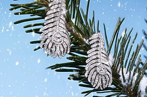 Diamond feather earrings hanging on a pine branch with a snowy background.