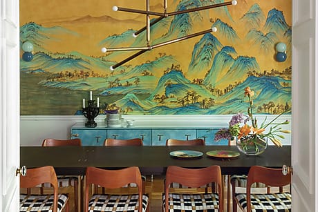 Dining room with mural of blue mountains, a modern chandelier, a dark table, wooden chairs, and floral centerpiece.