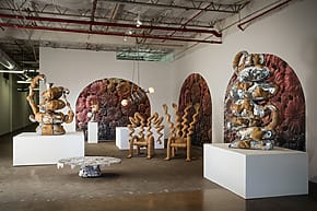 Art gallery installation featuring abstract sculptures on white pedestals and a floral patterned background wall.