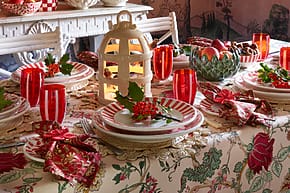 Festive dining table set with colorful plates, glasses, candles, and decorative foliage in an elegant, warmly lit room.