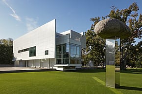 Modern art museum exterior with a grassy lawn and unique stone sculpture in the foreground under a clear blue sky.