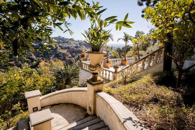 Scenic view from a Mediterranean-style terrace overlooking a lush valley with clear skies and distant hills.