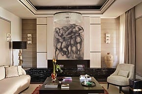 Elegant living room with modern art, large chandelier, stylish furniture, and decorative rug in warm neutral tones.