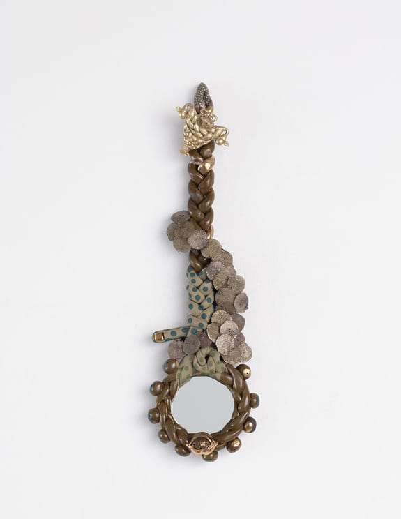 Decorative antique hand mirror with braided bronze handle and intricate floral ornaments against a white background.