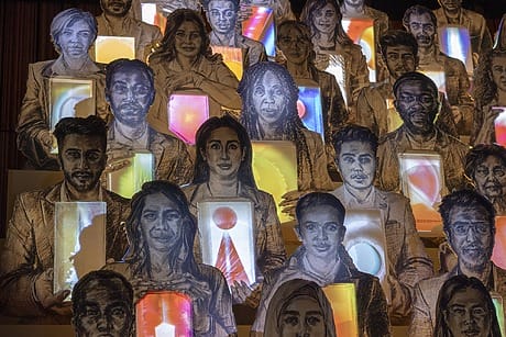 Art installation featuring diverse illustrations of people holding illuminated cubes with various geometric designs and colors.
