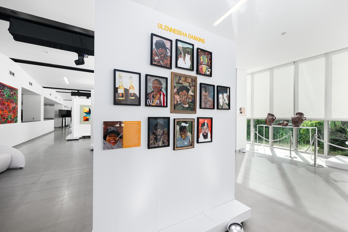 Art exhibit with various framed portraits displayed on a white wall in a modern gallery space.