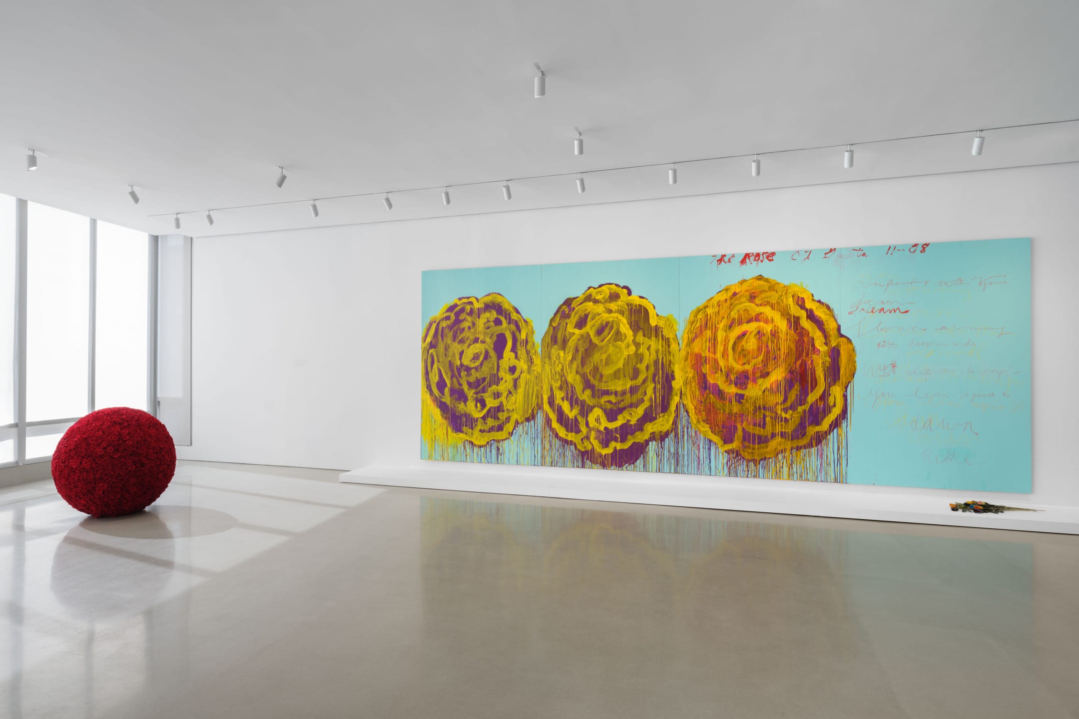 Contemporary art gallery with large turquoise canvas featuring three abstract yellow flowers and a red sphere sculpture.