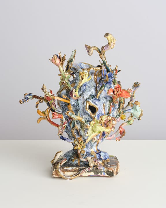 Colorful ceramic sculpture with abstract, organic shapes resembling flowers and branches on a white surface.