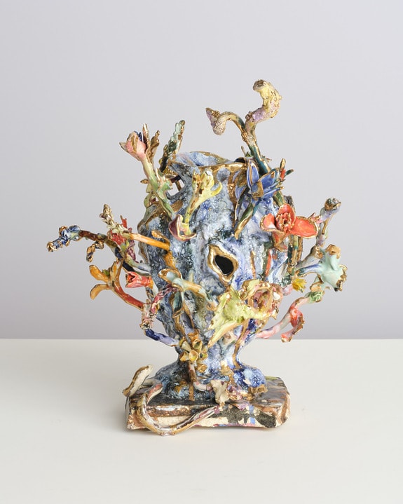 Colorful ceramic sculpture with abstract, organic shapes resembling flowers and branches on a white surface.