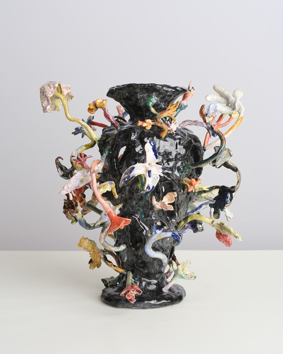 Black ceramic vase with colorful, abstract floral decorations on a simple white background.