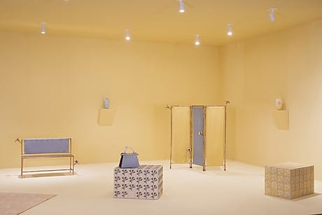 Minimalist yellow room with soft lighting, featuring unique furniture pieces and decorative vases on pedestals.