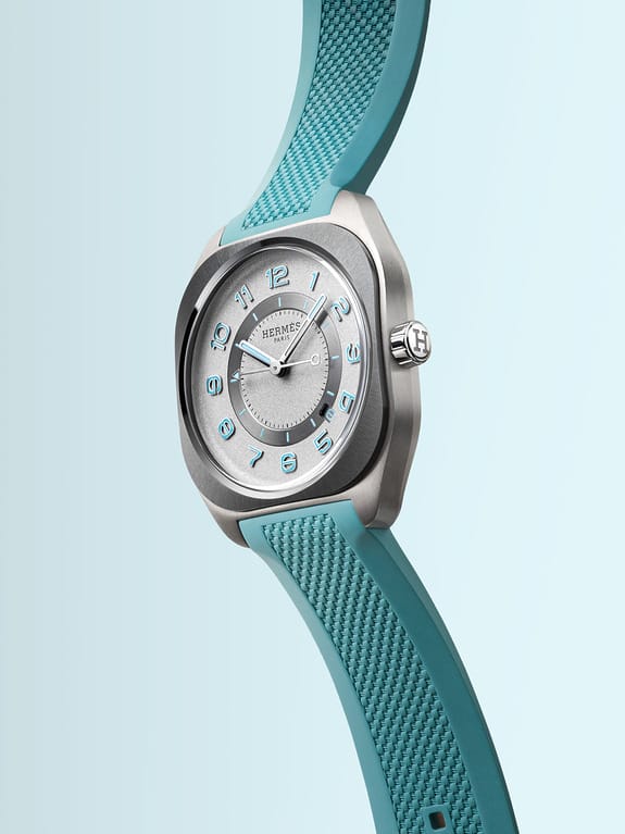 Silver watch with turquoise rubber strap, featuring a round dial with blue numerals on a light blue gradient background.