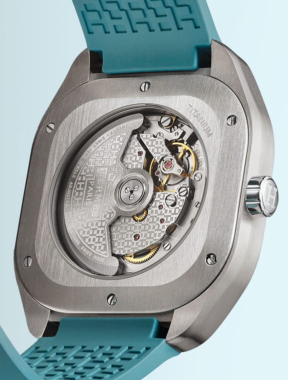 Back view of a luxury watch with visible intricate mechanical gears and a blue strap.
