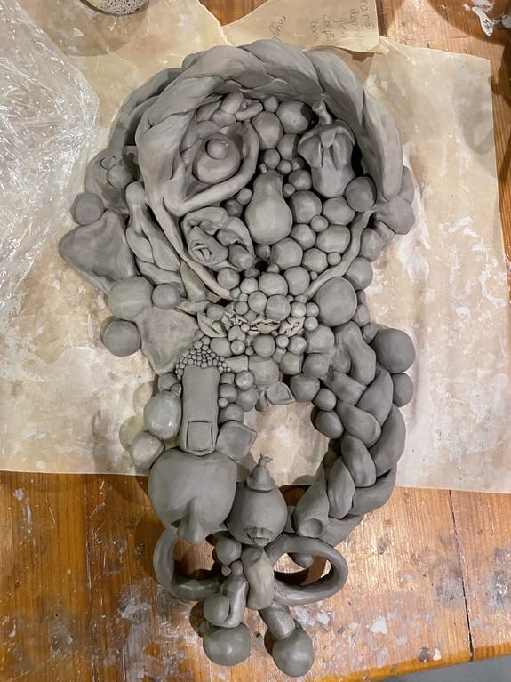 Clay sculpture with abstract shapes and textures, featuring various intertwined forms on a wooden surface.