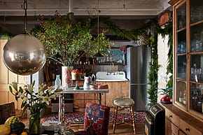 Eclectic kitchen with wooden cabinetry, floral decorations, colorful rugs, and vintage elements.