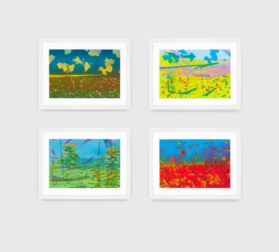 Four colorful abstract landscape paintings in white frames on a light gray wall.