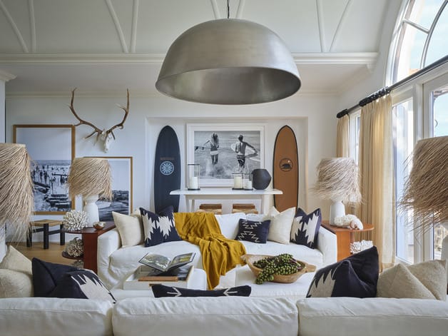 Coastal themed living room with surfboards, large pendant lamp, white sofa, decorative pillows, and antler wall decor.