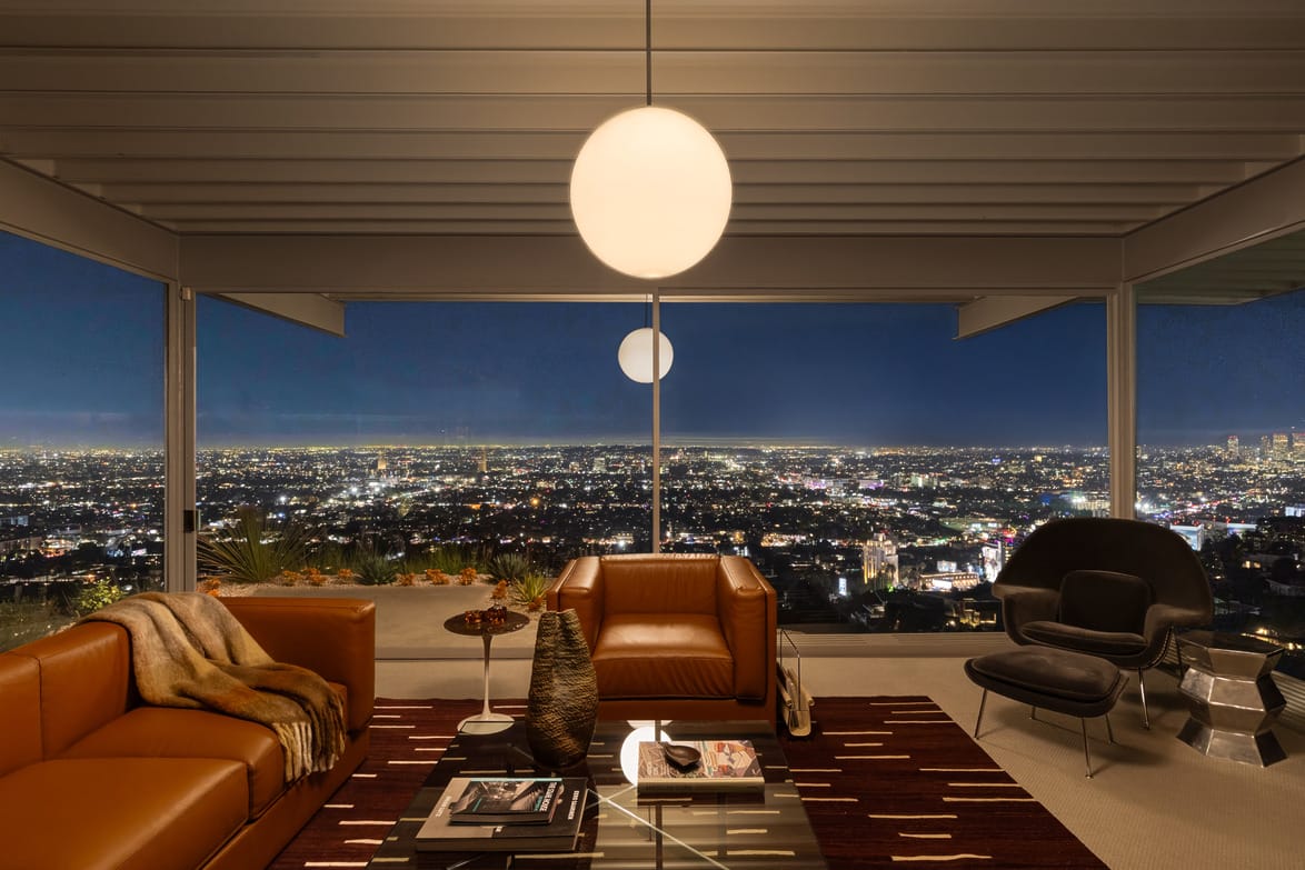 Modern living room with leather sofas and cityscape view through large windows at night.