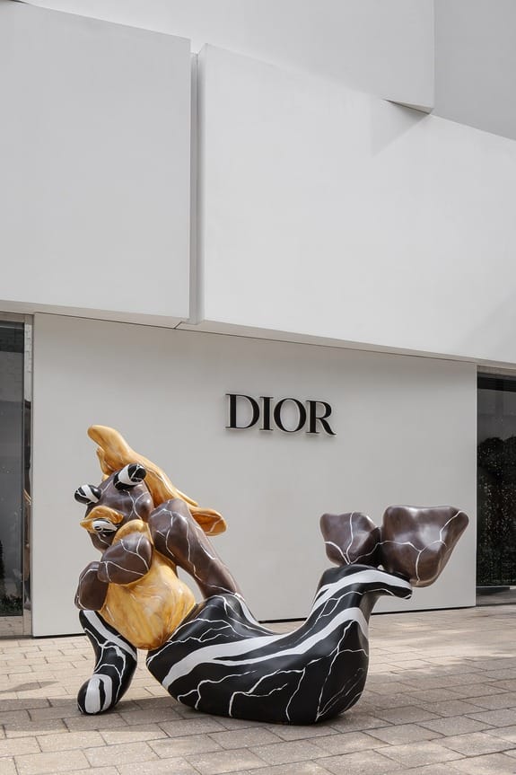 Abstract sculpture resembling a reclining figure in front of Dior store with a modern white facade.