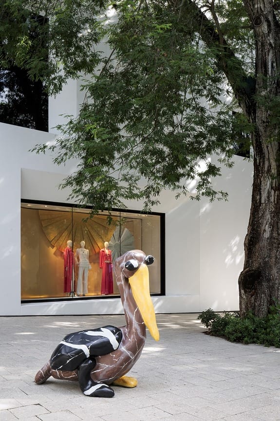 Sculpture of a bird with sunglasses in front of a modern building with mannequins dressed in red and white inside.
