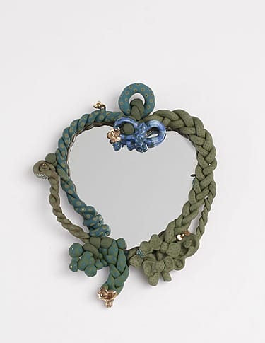 Heart-shaped mirror with braided green frame and blue decorative accents against a plain white background.