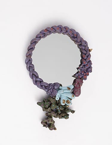 Colorful, intricately designed round mirror with purple braided frame and decorative clay accents at the bottom.