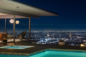 Modern house with pool overlooking a cityscape at night, featuring glowing city lights and clear night sky.