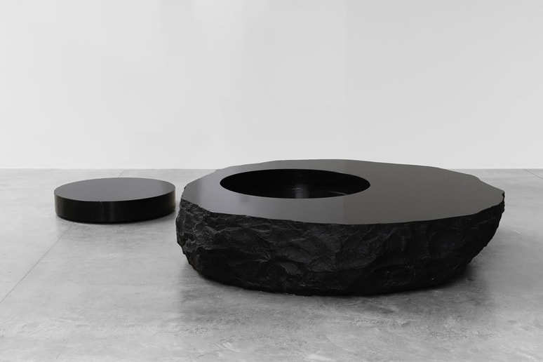 Modern black stone coffee table with a smooth top and rough edges against a minimalist, light gray backdrop.