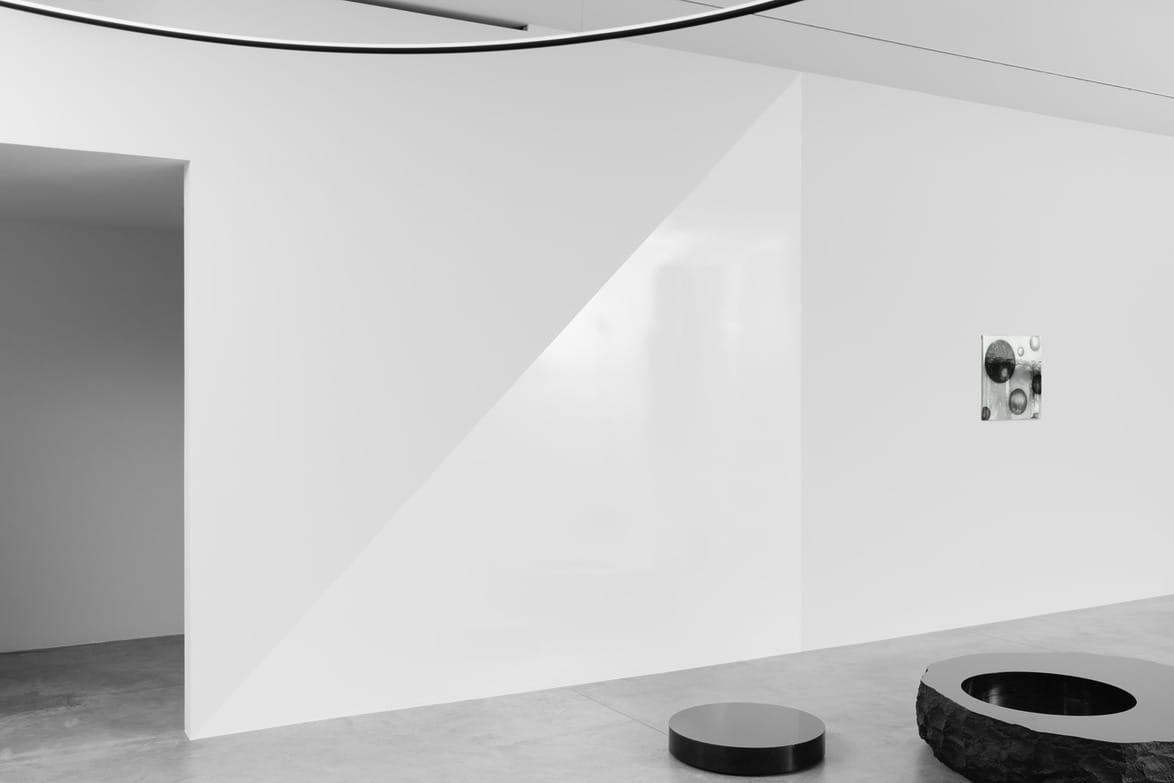 Minimalist art gallery interior with geometric shapes, featuring a black round bench on a concrete floor.