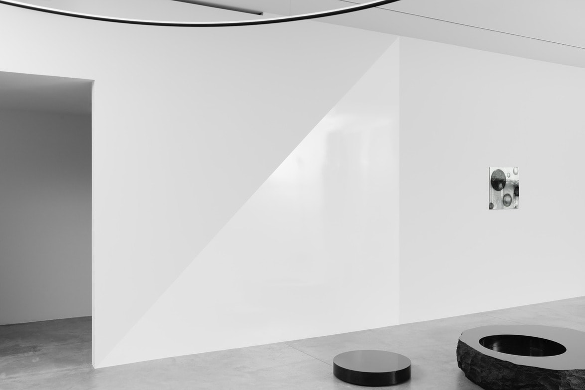 Minimalist art gallery interior with geometric shapes, featuring a black round bench on a concrete floor.