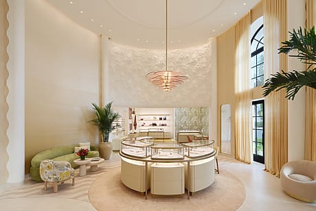 Luxurious jewelry store interior with elegant displays, plush seating, tall windows, and a modern chandelier.
