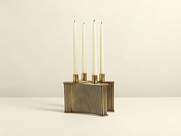 Gold candlestick holder with vertical grooves, holding three tall white candles on a neutral background.