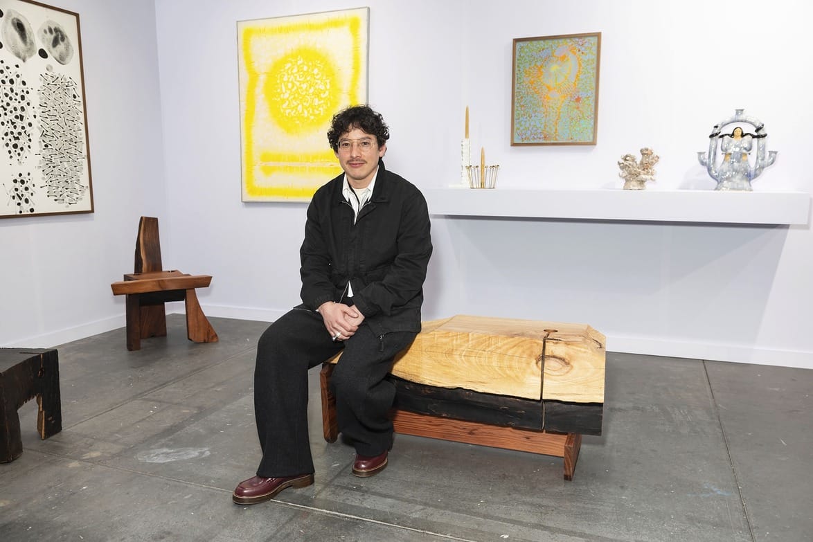 Person sitting on a wooden bench in an art gallery with abstract paintings and sculptures in the background.