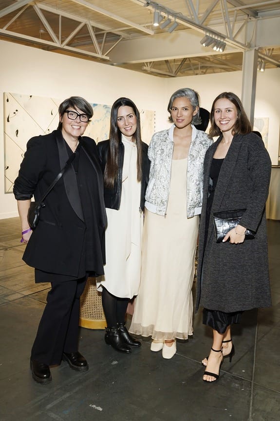 Four people smiling and posing together at an art gallery event, with paintings visible in the background.