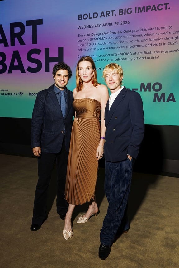Three people posing at an art gala event, standing in front of a colorful event backdrop and carpeted floor.