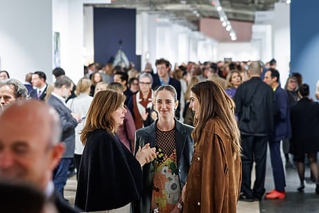 People socializing and walking through a bustling art gallery, engaging in conversations and viewing exhibits.