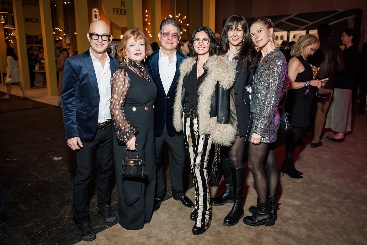 Group of people posing together at an indoor event, dressed in formal and stylish attire, with a lively background setting.