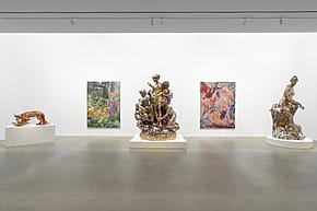 Contemporary art gallery with sculptures and paintings on display in a minimalist white room.