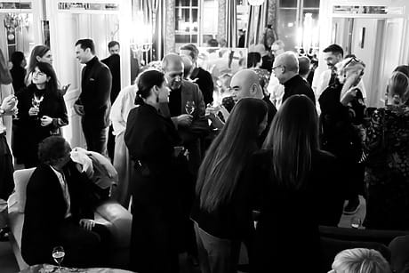 Black and white image of a crowded party where people are socializing, holding drinks, and engaging in conversation.
