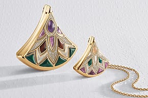 Gold and enamel pendant with intricate geometric design in green, purple, and white on a branded background